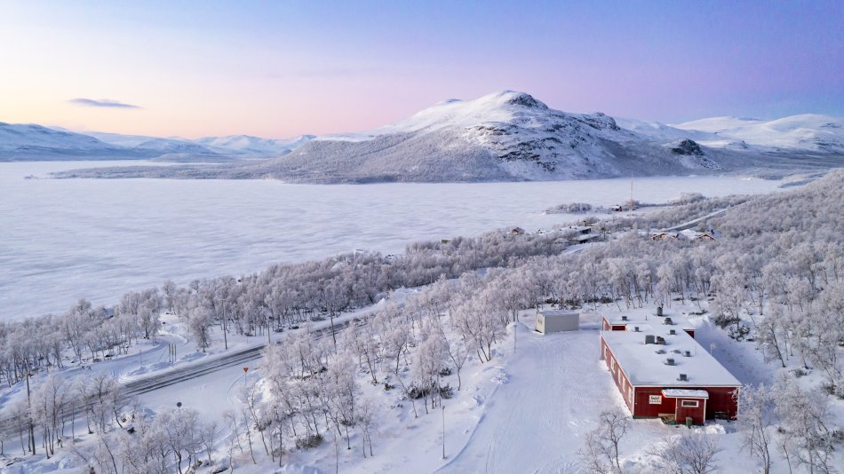 Hostel Saana pictured from above showing also the arctic nature around it on a frosty winter day. Lake Kilpisjärvi and fell Pikku-Malla can be seen on the background.