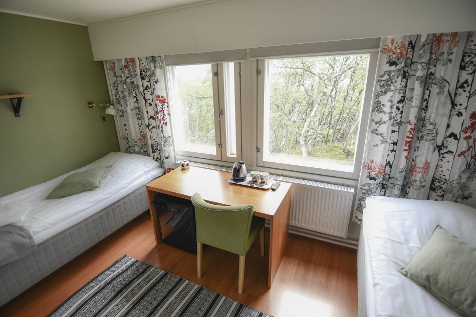 Twin room in Kilpisjärven Retkeilykeskus. Two beds, a desk, chair, tv and a fridge.